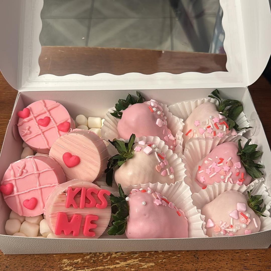 Valentine's mixed box with decorated Oreos including a tic-tac-toe heart design and KISS ME text, plus pink strawberries with Valentine's sprinkles.