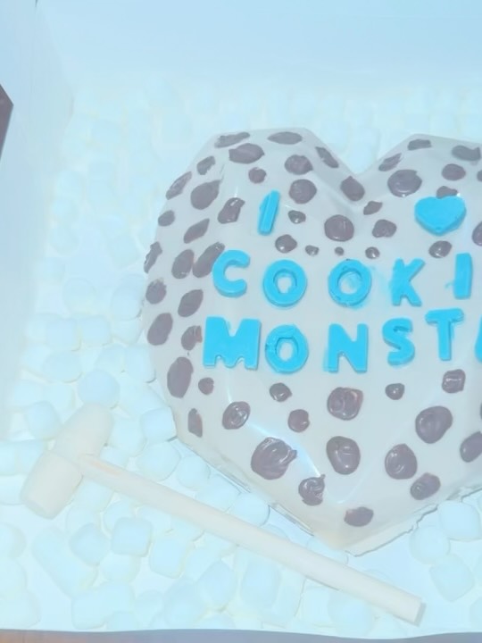 Close-up of a Cookie Monster-themed geometric faceted breakable chocolate heart with chocolate chip dot texture, nestled on a bed of mini marshmallows.