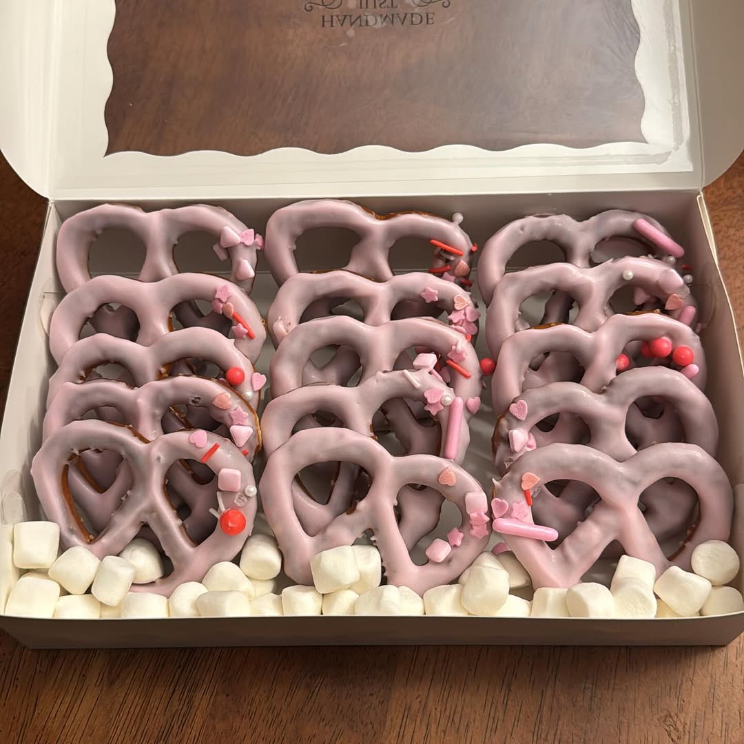 Large box densely packed with lavender chocolate-covered pretzels topped with Valentine's heart and star sprinkles in pink and red.
