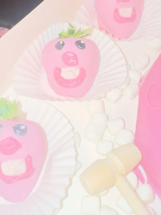 Close-up of whimsical pig-face strawberries dipped in bright pink chocolate with expressive eyes, snouts, teeth, and round ears.
