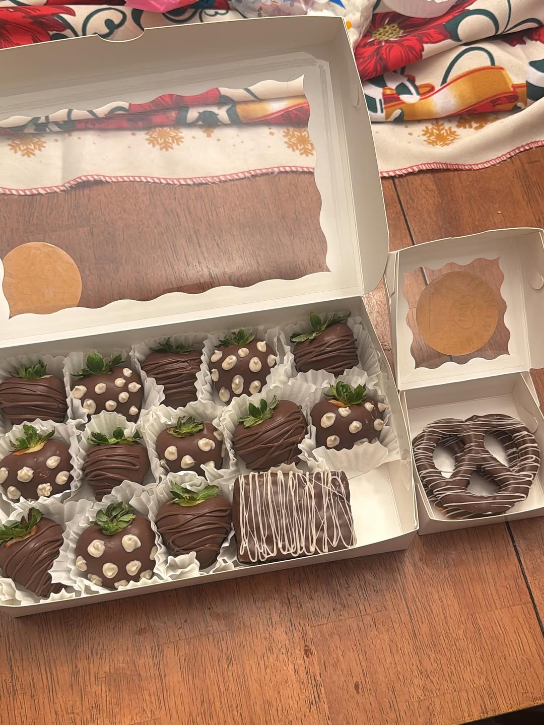 Chocolate-covered strawberries with white chocolate chip polka-dot pattern and drizzle, plus a pretzel, with a holiday poinsettia tablecloth visible behind.