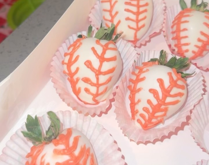 Close-up of white chocolate strawberries with detailed orange piped baseball stitching resembling real baseballs.