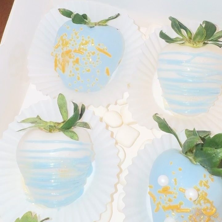 Close-up of baby blue chocolate strawberries with scattered gold foil flakes, fine white drizzle, and sugar pearls for an upscale luxurious look.